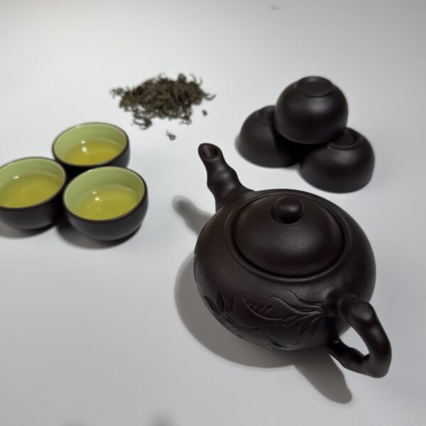 Zisha-Tonteekanne und Tassen neben losem Thai-Nguyen-Grünteeblatt