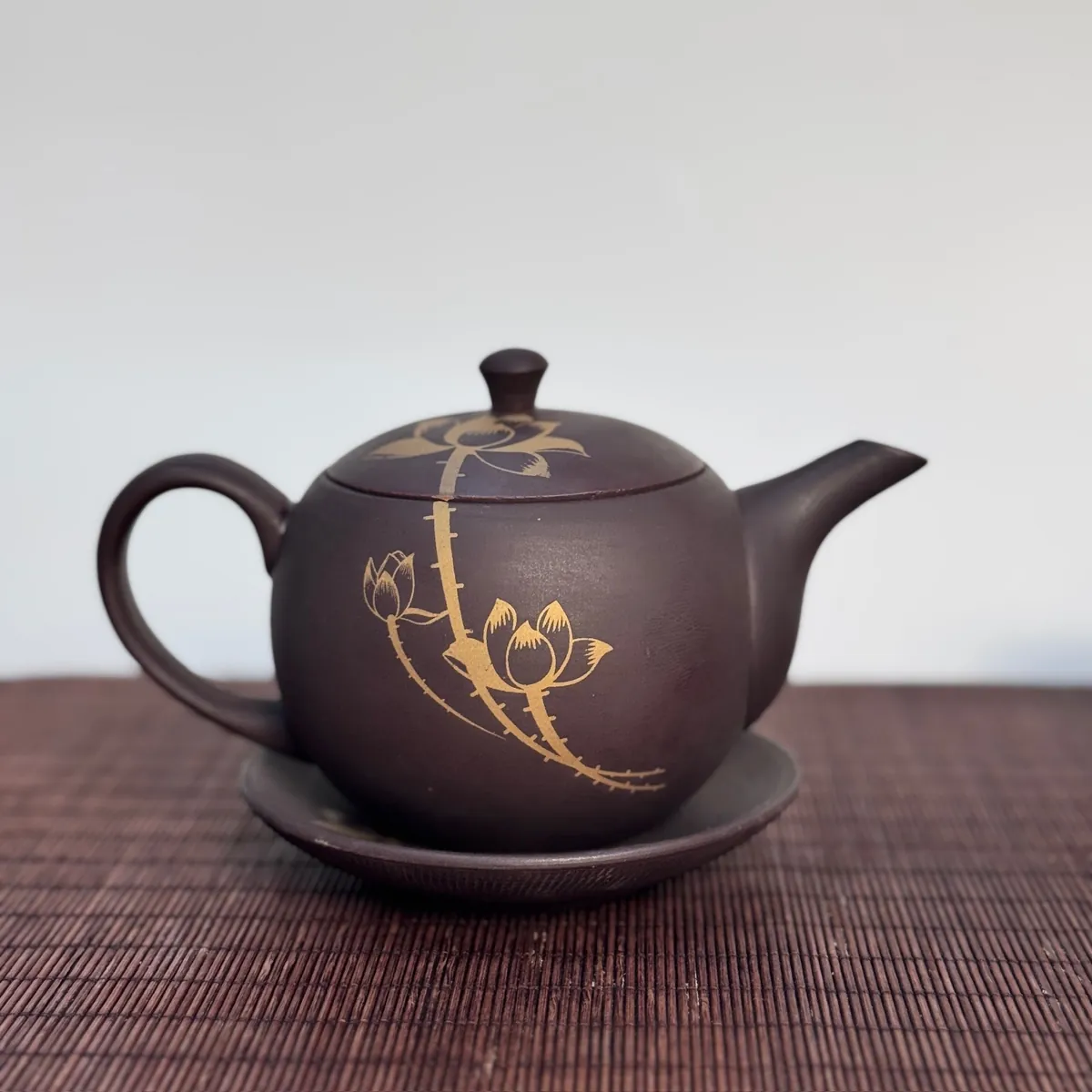 Luc Am Kim Lien zisha teapot hand-painted with golden lotus, resting on its saucer – TRAVINA