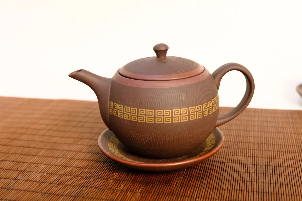 Luc Am Quan Anh zisha teapot with gold seal-script pattern on its saucer, bamboo mat background – TRAVINA
